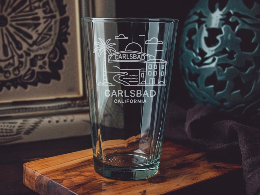 Carlsbad California Pint Glass with Ocean View, Beach Scene, Palm Trees, and Coastal Landmarks Design