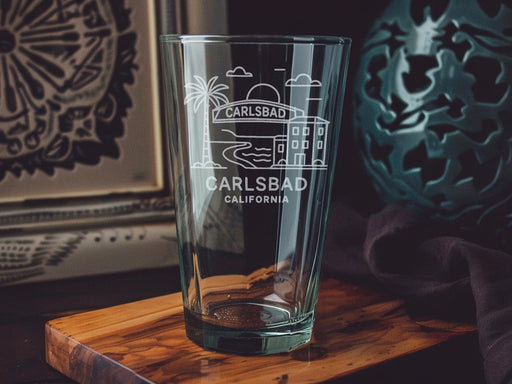 Carlsbad California Pint Glass with Ocean View, Beach Scene, Palm Trees, and Coastal Landmarks Design